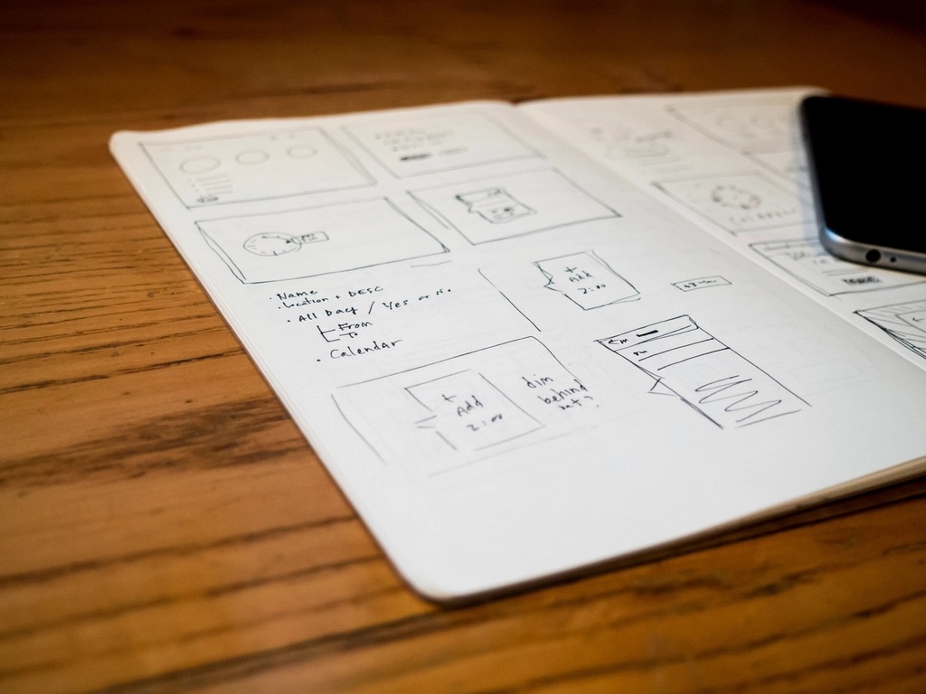 Hand-drawn mobile app wireframes in a sketchbook next to a smartphone
